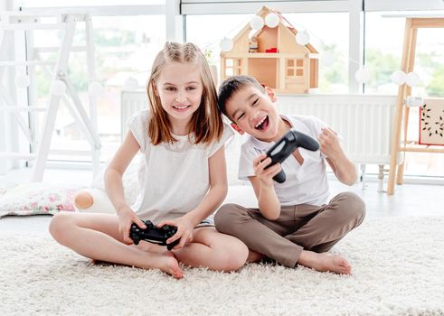 Cute little girl and boy with joysticks playing on console indoors