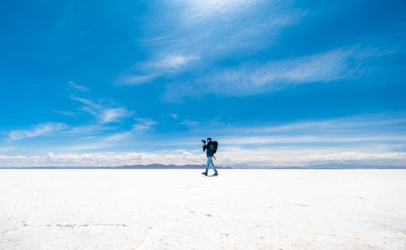 Tourist with equipment and camera walking in sunshine Salar de Uyuni