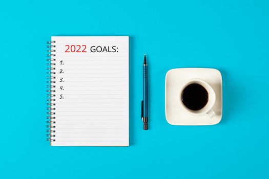 2022 goals concept banner. Notebook, pencil and a cup of black coffee isolated on blue background