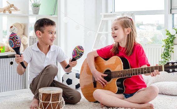 Smiling kids playing on drum and guitar in modern apartment