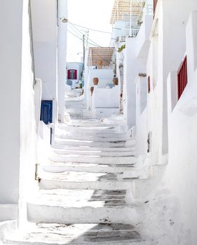 Beautiful narrow street with white houses in Mikonas island, Greece. Traditional narrow street with white facedes of buildings and blue doors