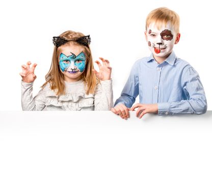 Beautiful little girl and boy with painted faces holding a blank board for text or advertising isolated on white background. Cat and dog face art for kids
