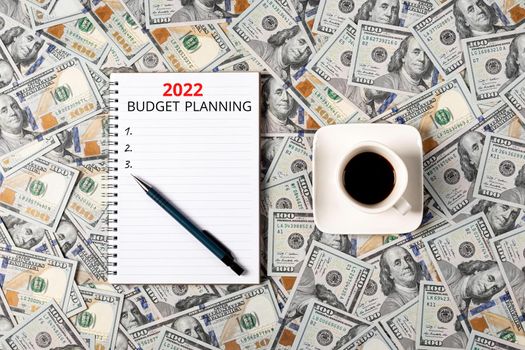 2022 budget planning banner with copy space. Notepad, pen and a cup of black coffee isolated on money background. Notepad with copy space. Office, business, discreet style