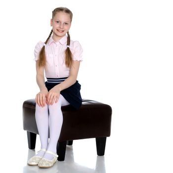 Beautiful schoolgirl girl with long pigtails sitting on the couch. The concept of school fashion, children's emotions. Isolated on white background.