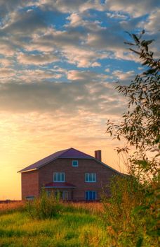 red brick house in the field of yellow flowers with cloudy sky in background