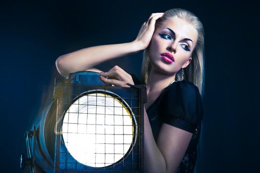 Sexy young woman with old floodlight over dark background