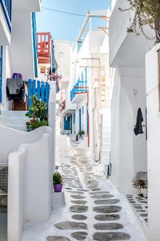 Beautiful narrow street with white houses in Mikonas island, Greece. Traditional narrow street with white facedes of buildings and blue doors
