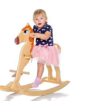 Little girl swinging on a wooden horse. The concept of a happy childhood, games in kindergarten and in the family. Isolated against white background.