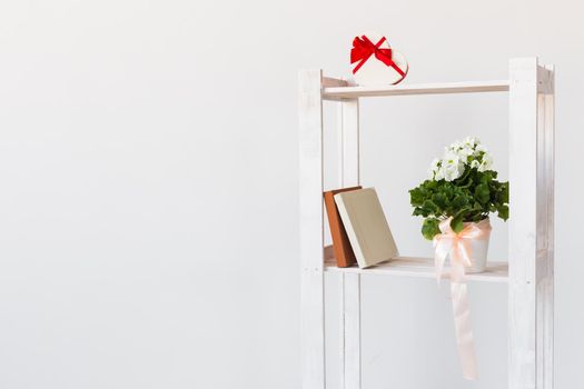 Heart shape gift box and books and indoor plant on a bookshelf. Minimal composition. Spring interior concept