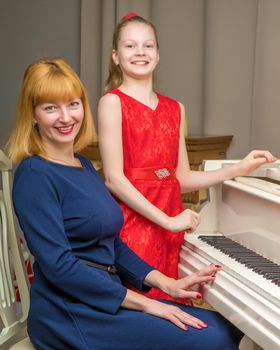 A beautiful young mother with a little daughter near a large white grand piano. The concept of family happiness, music education.