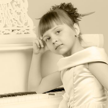 Fashionable little girl in a stylish beautiful dress.The girl is playing on a large white piano.