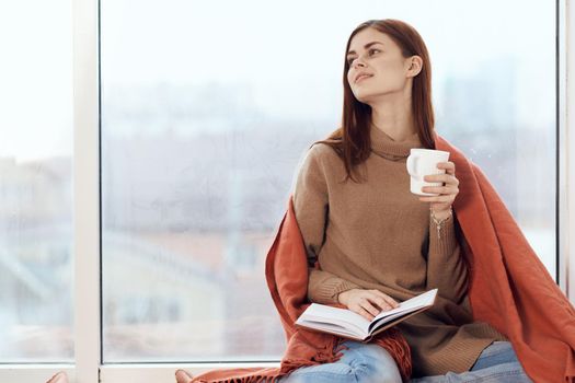 woman with a cup of drink on the windowsill reading a book rest morning. High quality photo