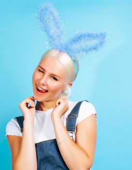 young pretty blond girl with rabbit ears posing cheerful on blue background, lifestyle people concept close up