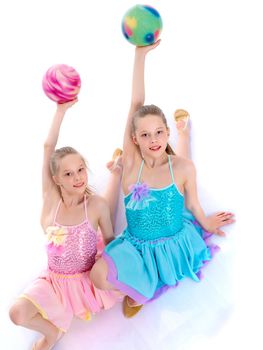 Two cute gymnast girls are sitting on the floor in a studio on a white background. The concept of children's sports, fitness. Isolated on white background.