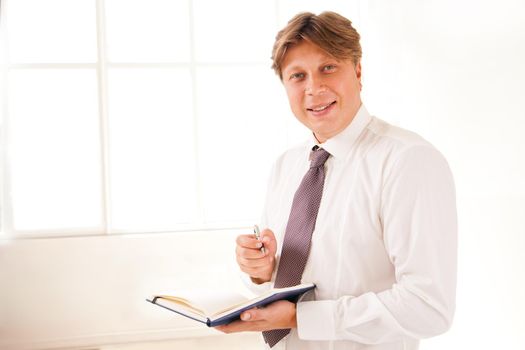 Smiling Businessman standing in office holding diary on white