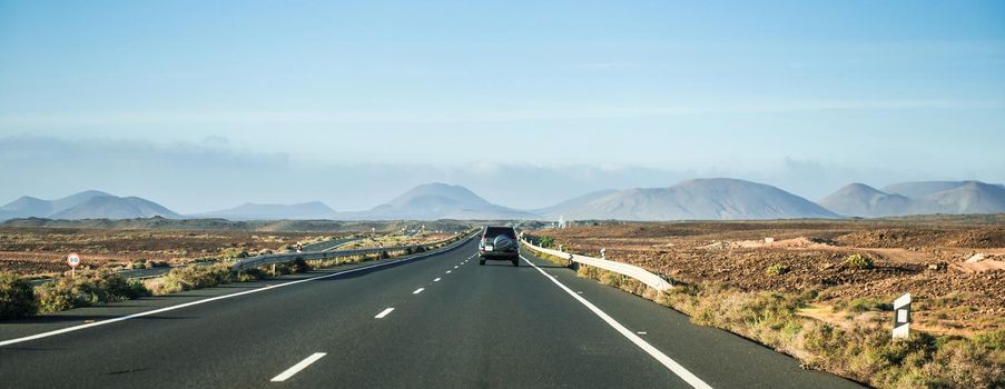 car driving away on road to mountains in Canary Island desert, Lanzarote, Spain, panorama