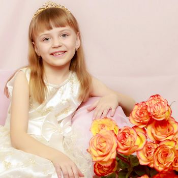 A beautiful little princess with long, light, flowing hair, in an elegant long white dress.With a bouquet of beautiful tea roses.