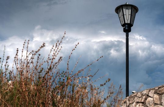 street lantern on the rocky ground with bush in foreground and dramatic blue sky in background