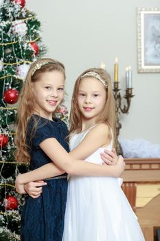 Adorable little twin girls hugging each other near the Christmas tree.