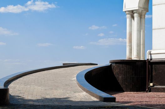 colonnaded entrance to the building with pathway in foreground and blue cloudy sky in background