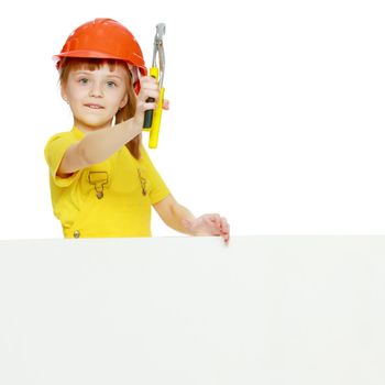 A nice little girl in a construction helmet and a yellow T-shirt peeped out from behind a white advertising banner.Girl in a construction helmet peeks out from behind a billboard.