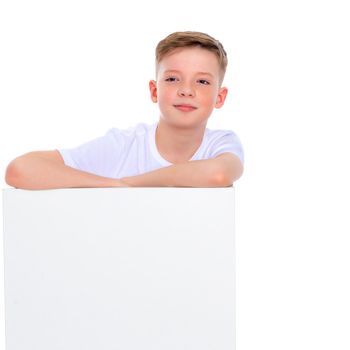A handsome school-age boy near a white advertising banner. On the banner it is possible to write any advertising text. The concept of promotion of goods and services. Isolated on white background.