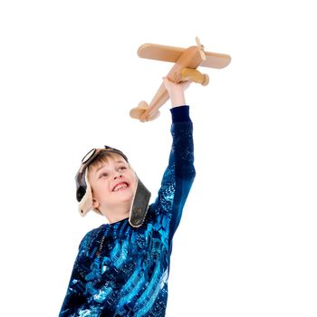 The boy in the helmet of the pilot plays with a toy wooden plane. He dreams of becoming a pilot. Concept of happy childhood, child in the family.Isolated on white background.