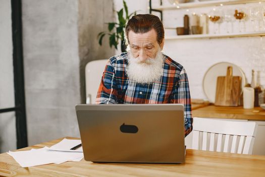 Old man with laptop. Grandfather sitting in a Christmas decorations. Man in a cell shirt.