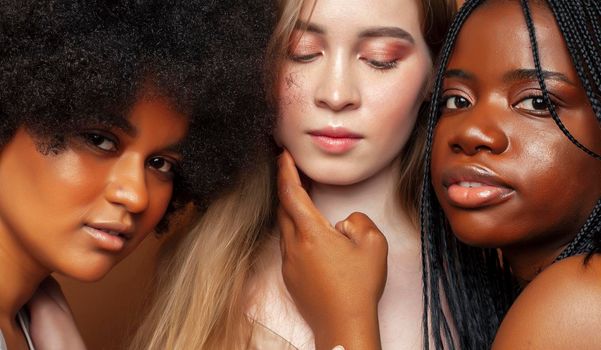 young pretty african and caucasian women posing cheerful together on brown background, lifestyle diverse nationality people concept close up