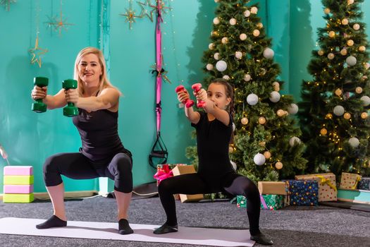 mother and daughter doing fitness exercises on warm floor near Christmas tree at home