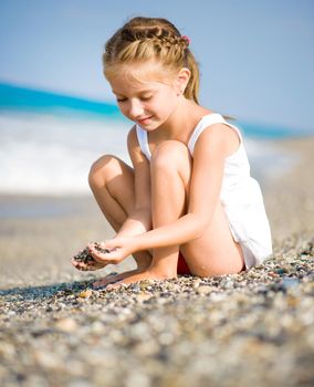 Seated girl with pebbles in her hands on the beach