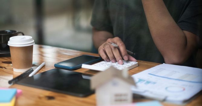 Man calculating financial chart for investment to buying property with house model. Male using calculator for house loan.