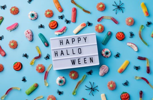 Halloween concept. Halloween party decorations with lightbox with words Happy Halloween, sweets, pumpkins top view flat lay on blue background