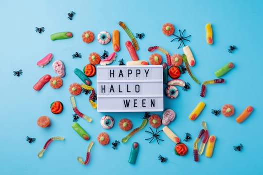 Halloween concept. Halloween party decorations with lightbox with words Happy Halloween, sweets, pumpkins top view flat lay on blue background
