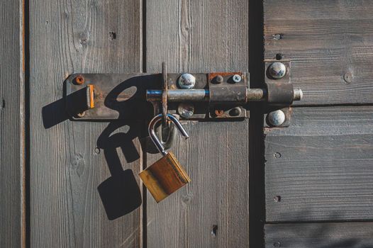 Brass padlock with bolt lock on wooden door.