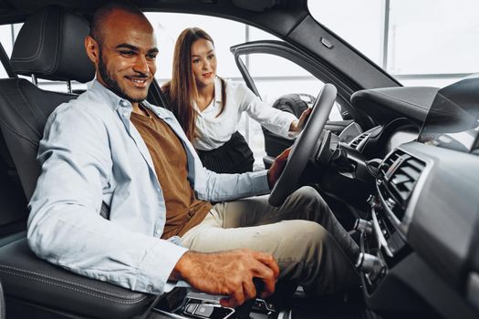Young attractive caucasian woman salesperson in car showroom showing a car to her male African American client