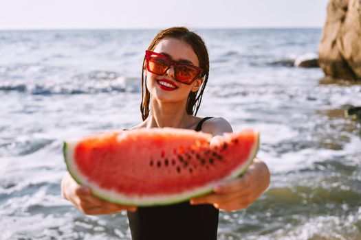 cheerful woman in sunglasses eating watermelon by the ocean. High quality photo