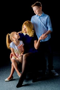 Beautiful young mother with her son and daughter in the studio on a black background. The concept of a family portrait, a friendly family.