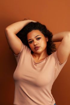 pretty young african american woman with curly hair posing cheerful gesturing on brown background, lifestyle people concept close up