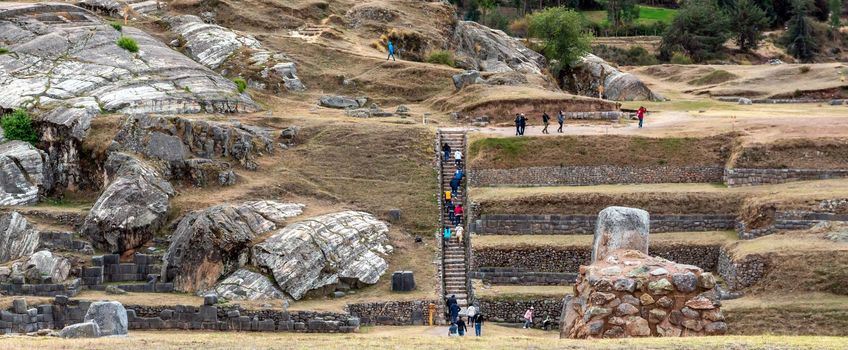 In the village Saksaywaman groups of tourists are sightseeing the ruins of aged ruins of stone citadel