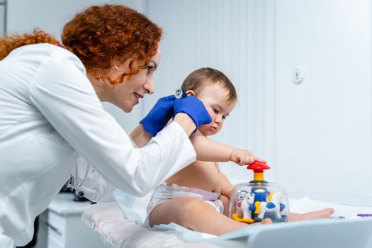 Pediatrician doctor concept. Children medical care. One year old baby girl examined by female pediatrician in clinic office. Child visiting doctor for health check-up. Doctor examine little patient.