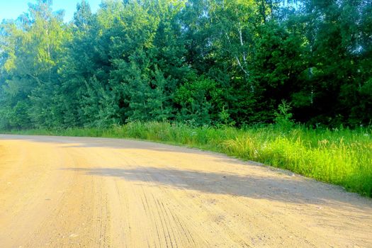 Gravel road on a sunny summer day leading happiness. Relaxing walk along the path. Near the village and summer vacation.