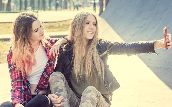 Cheerful smiling teen girls taking selfie in the skatepark. Girls in trendy outfits making selfie