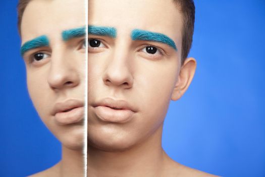 Handsome male with creative make-up and reflection in mirror over blue background