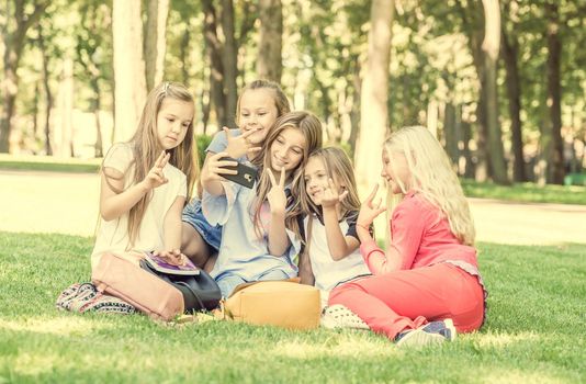 Beautiful teens sitting on the grass in the park and taking cute friendly selfie