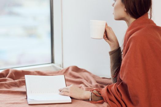 woman near the window with a plaid reading a book rest. High quality photo