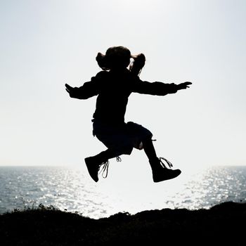 silhouette of a little girl jumping on a background of the sea at sunset