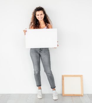 Cute girl standing near frame with empty canvas in her hands