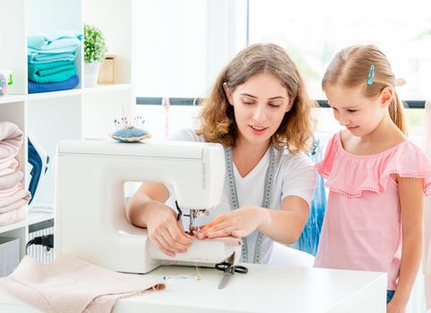 Little girl is taught to sew by teacher at class