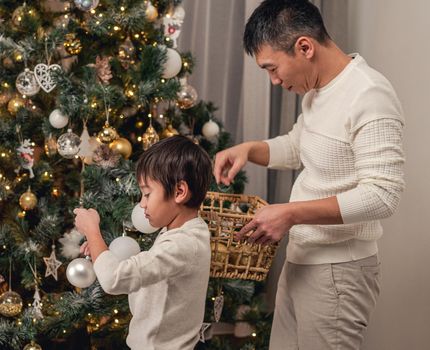 Little son and father decorating christmas tree for holidays at home